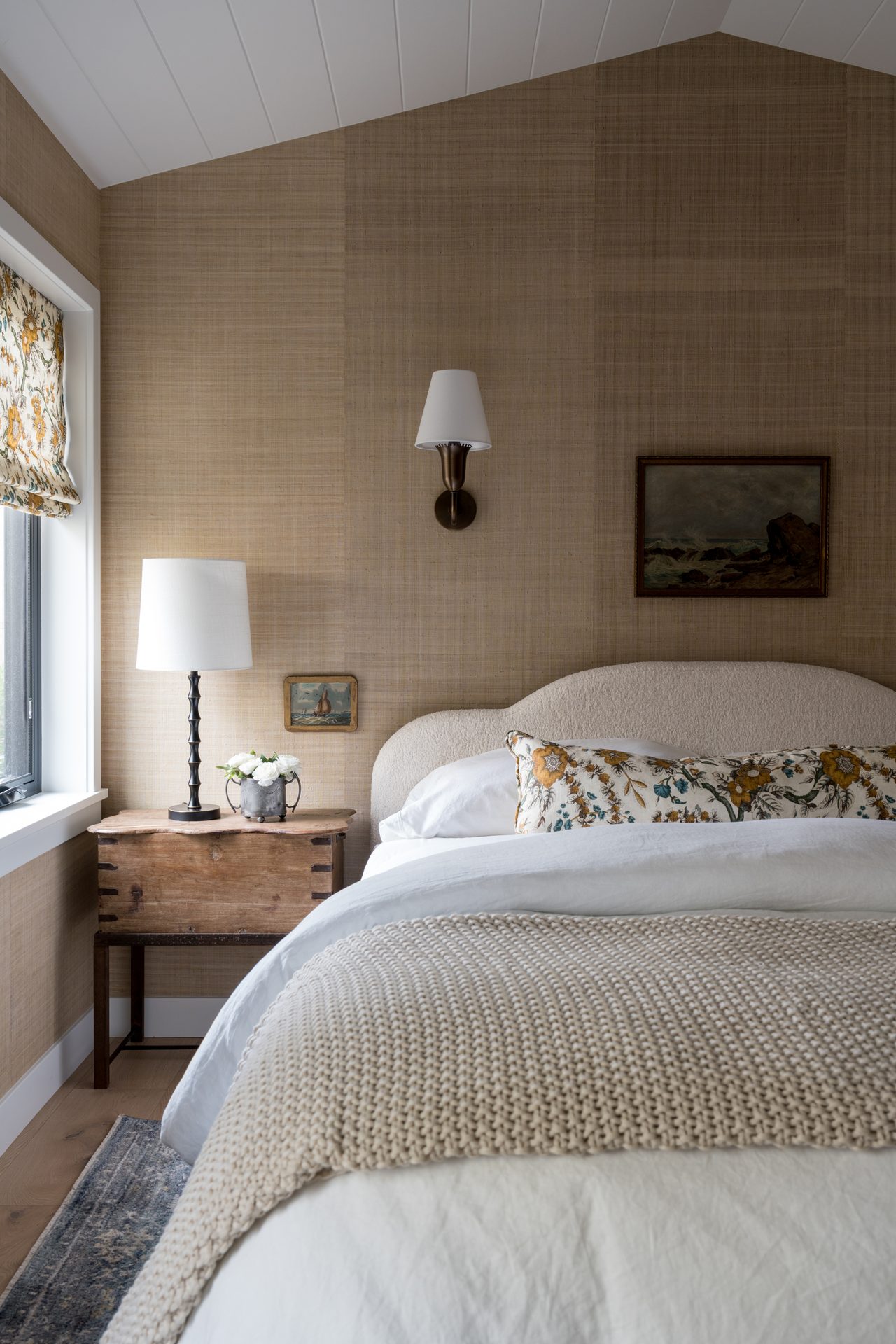 Bedroom with layered bedding, textured wall covering, bedside lighting, and warm natural light